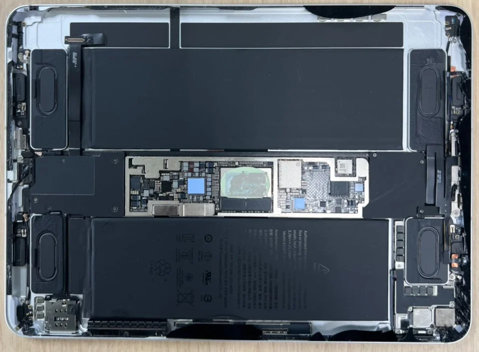 タブレットの内部構造が詳細に写された画像。2つの大型バッテリー、中央のロジックボード、スピーカーモジュールなどの精密な電子部品が確認できる。