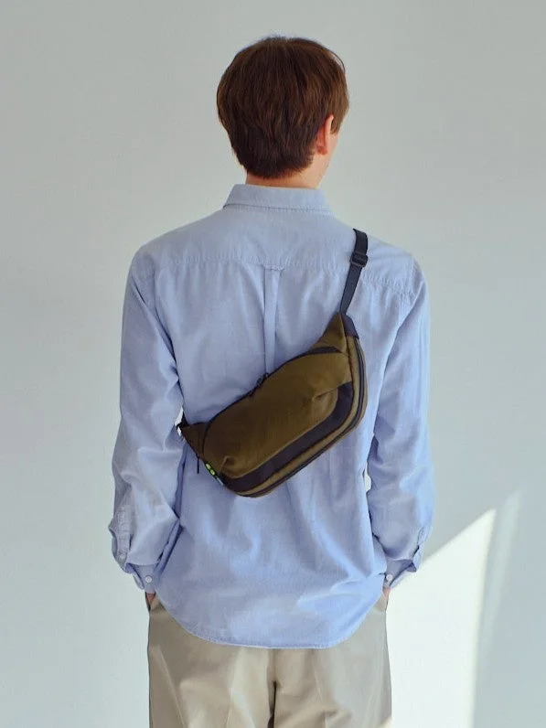 ライトブルーのシャツとベージュのパンツを着用し、カーキ色のボディバッグを斜め掛けにした男性の後ろ姿