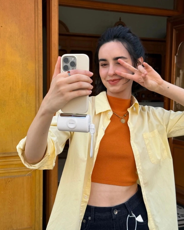 若い女性がスマートフォンで自撮りをしており、ピースサインをしながら笑顔を見せています