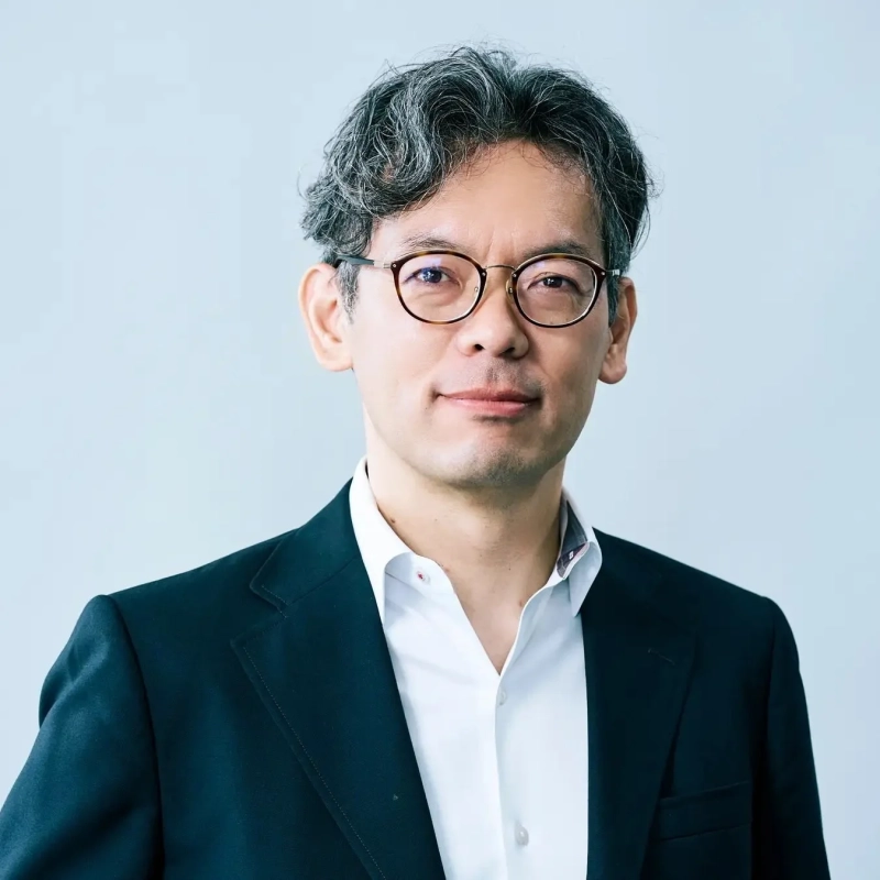 グレーの巻き毛と眼鏡をかけた中年男性がカメラをまっすぐ見つめているポートレート