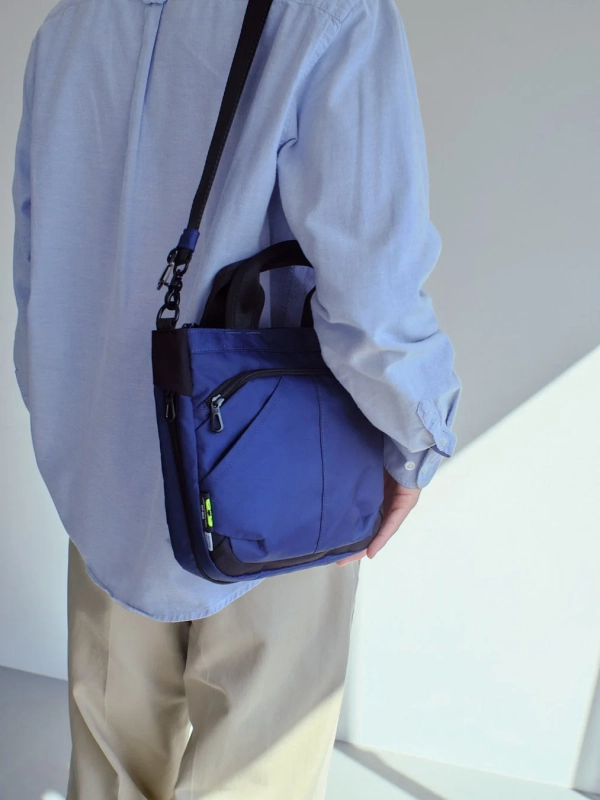 水色のシャツとベージュのパンツを着た人物が青いショルダーバッグを身につけている