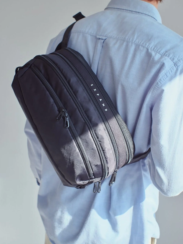 水色のシャツを着た人物が黒いボディバッグを背負っている後ろ姿