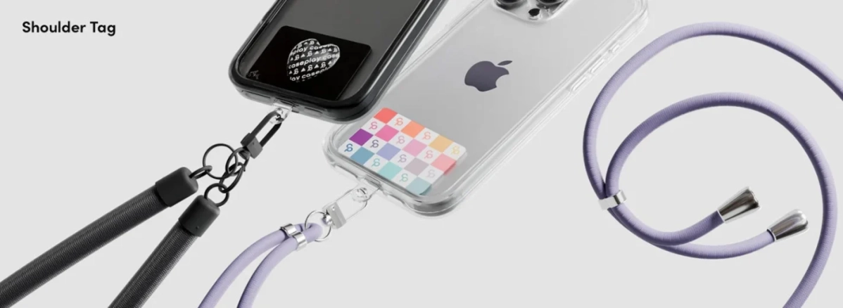 スマートフォンにショルダーストラップとケースを装着した様子を捉えた画像です。黒いケースには黒いストラップ、クリアケースにはラベンダー色のストラップが取り付けられており、それぞれ異なるデザインのタグが挟み込まれています。