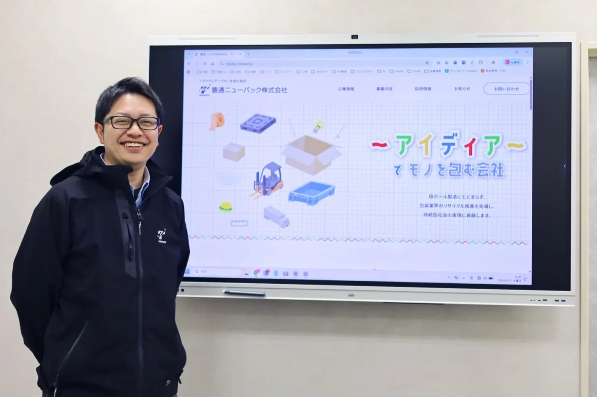 豊通ニューパックのウェブサイトが表示された大型スクリーンと男性