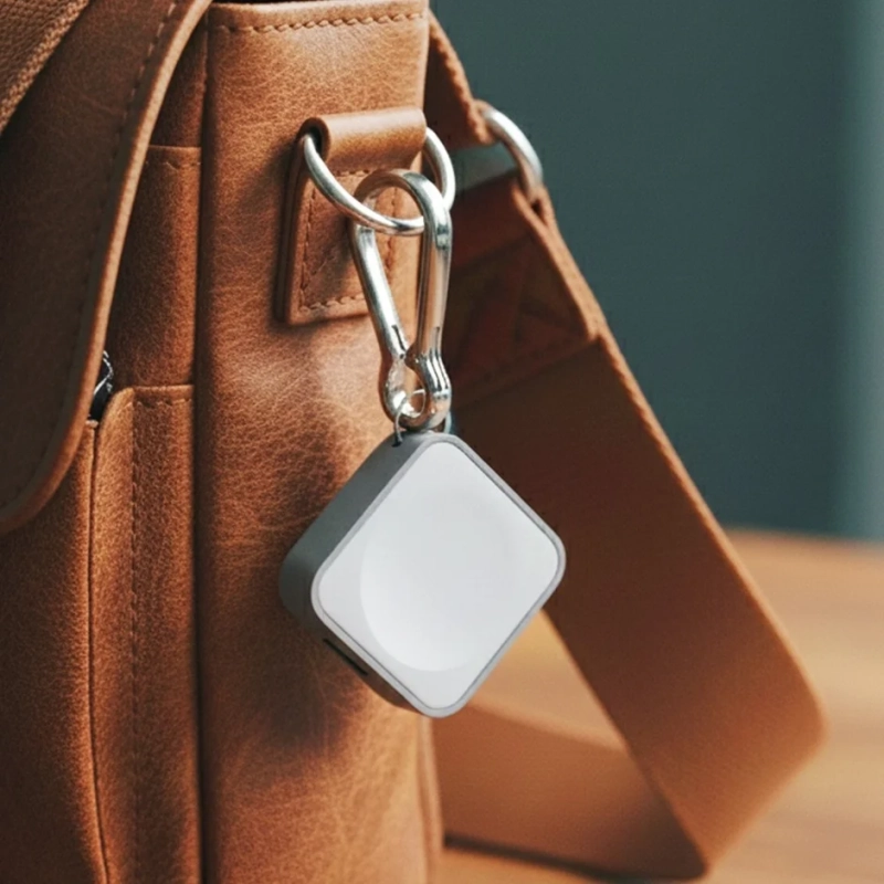 茶色のレザーバッグに銀色のカラビナで取り付けられた、白とグレーの四角い小型電子機器が写っています。