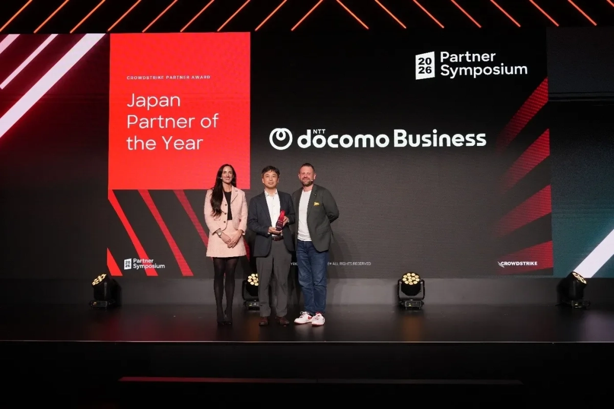 CrowdStrikeのパートナーアワードでNTTドコモビジネスが「Japan Partner of the Year」を受賞した際の表彰式の様子です。ステージ上で3人の人物がトロフィーを持ち、笑顔で立っています。
