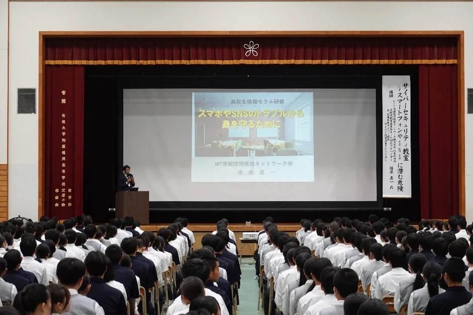 高校生を対象とした情報モラル研修の様子です。講師が「スマホやSNSのトラブルから身を守るために」と題して講演しており、多くの生徒が熱心に耳を傾けています。サイバーセキュリティに関する重要なテーマが扱われています。