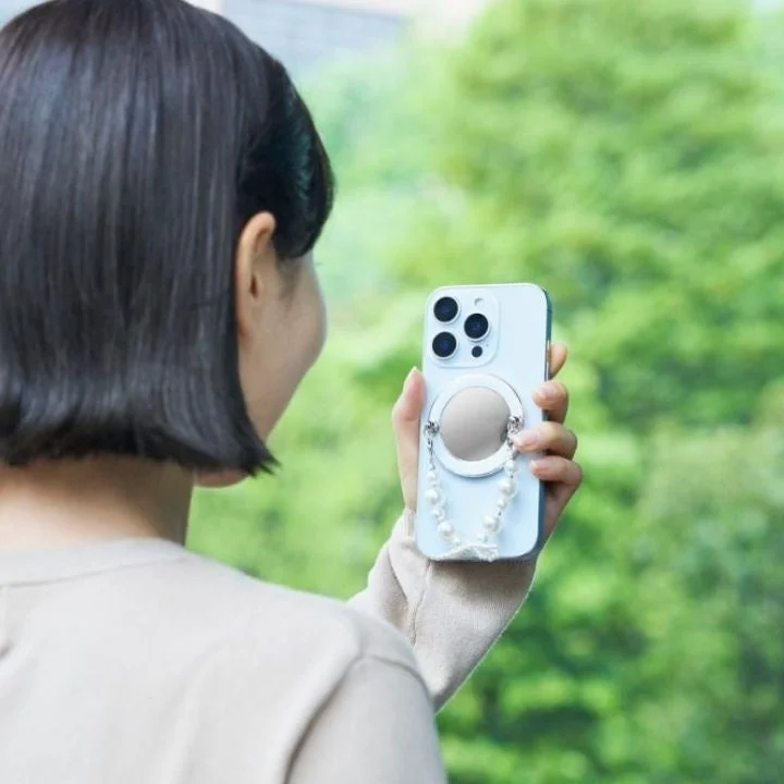 パールストラップとミラー付きスマートフォンを持つ女性の後ろ姿