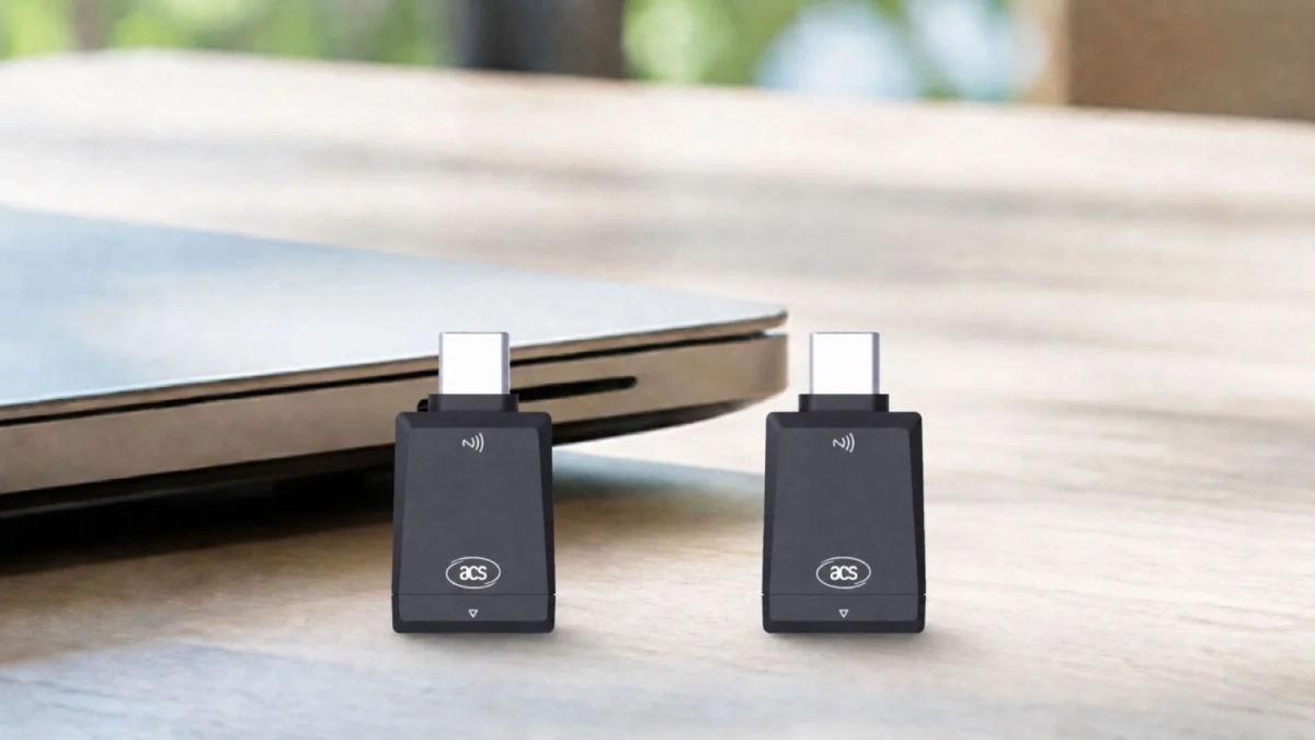 2つの黒いUSB-Cワイヤレスアダプターが、ノートパソコンの隣の木製テーブルに置かれています。無線通信機能を備えた小型デバイスです。