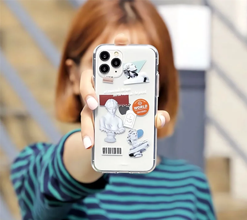 女性が石膏像や「WORLD」の文字がデザインされたクリアなiPhoneケースを装着したスマートフォンを持っている様子