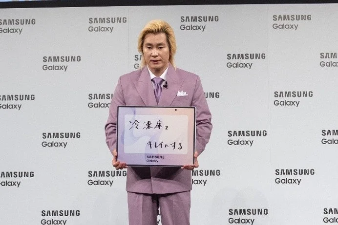 紫のスーツを着た金髪の男性が、「冷蔵庫をキレイにする」と書かれたタブレットを掲げている