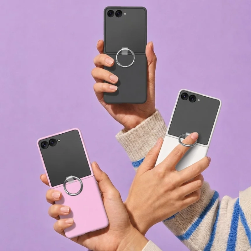 紫色の背景をバックに、複数の手がリング付きケースを装着した折りたたみスマートフォン（黒、ピンク、白/グレー）を持っている様子。カラフルなスマホアクセサリーが強調されています。