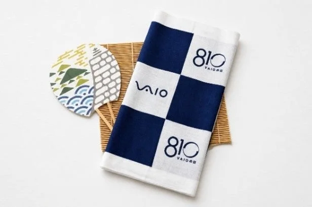 VAIOのロゴと数字「810」がデザインされた青と白の市松模様のタオルと、伝統的な和柄の扇子