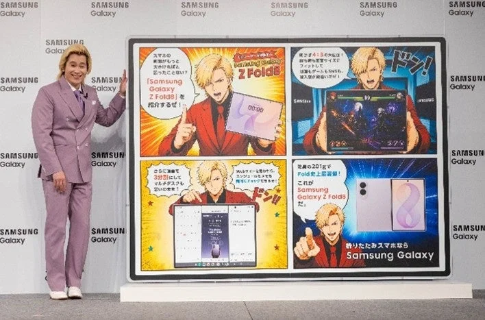 紫のスーツを着た男性が、Samsung Galaxy Z Fold8の漫画風広告パネルを紹介している