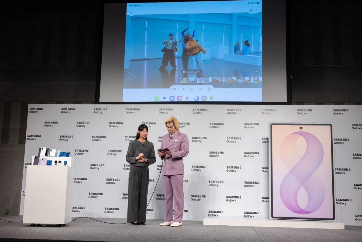 SAMSUNG Galaxyの新製品発表会と思われるイベントの様子です。ステージ上では2人のプレゼンターが製品について説明しており、背後の大型スクリーンには動画が映し出されています