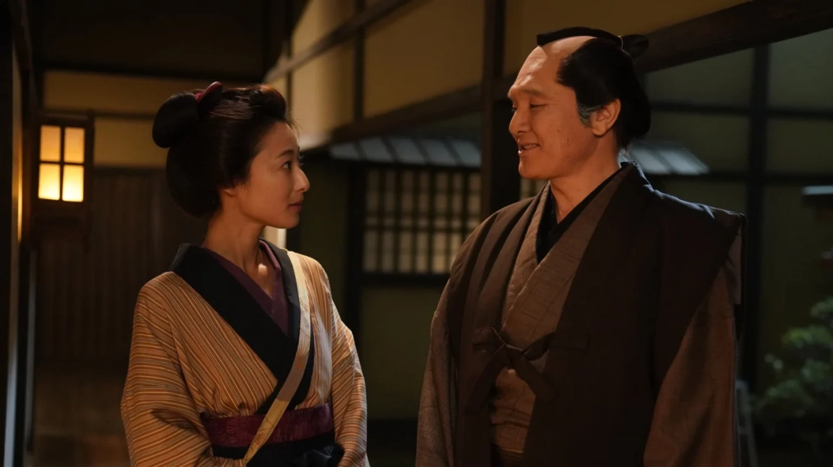 伝統的な和装を身につけた男女が、薄暗い日本家屋の中で向かい合い、真剣な表情で会話を交わしている様子。時代劇の一場面のようです。