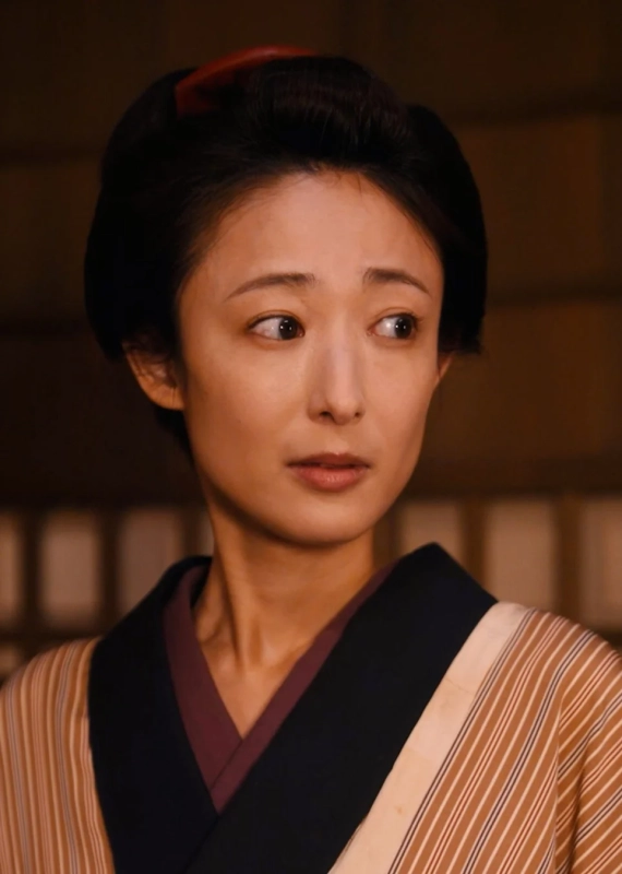 伝統的な和服を身につけ、髪に赤い飾りをつけた日本人女性のポートレート。彼女はやや驚いたような、または真剣な表情で右方向を見つめている。背景は日本の家屋を思わせる。