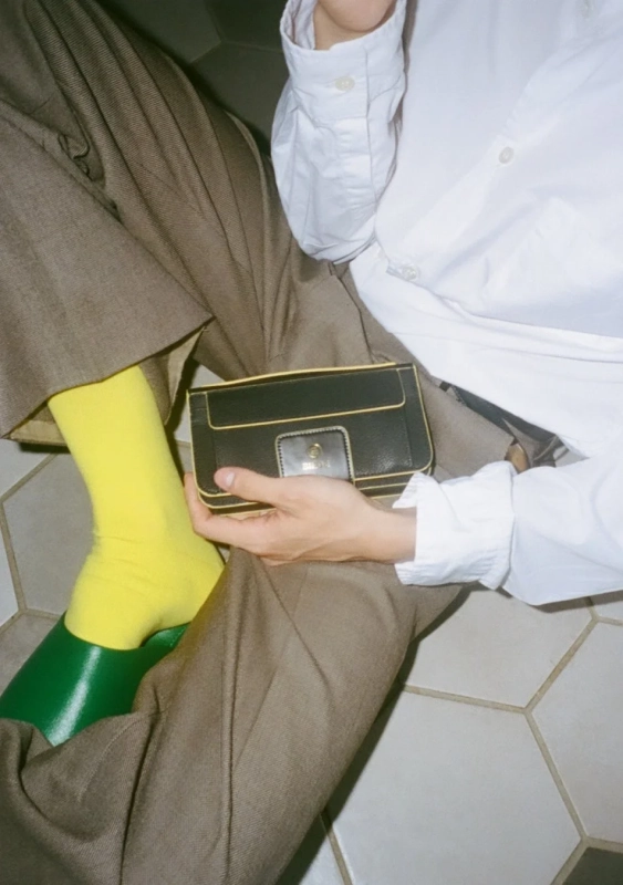 茶色のパンツに鮮やかな黄色のソックスと緑色の靴を合わせ、黒と黄色のミニバッグを持つ人物のクローズアップ画像